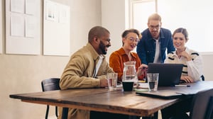 Four people in a small conference room gathered around a laptop