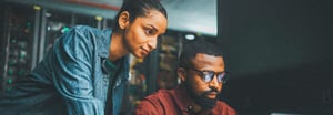 Two people in a server room looking at a computer monitor