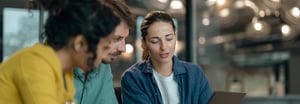 Three colleagues collaborating around a laptop in a modern office setting